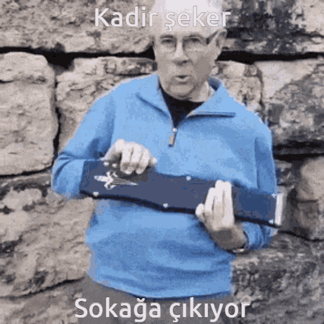 a man in a blue shirt is holding a knife in front of a stone wall