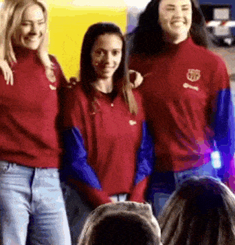 a group of three women are standing next to each other in front of a crowd .