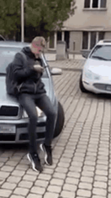a man is sitting on the hood of a car while looking at his phone .