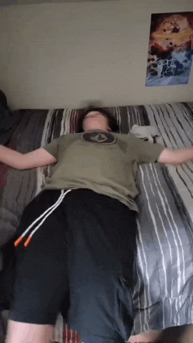a man laying on a bed with his arms outstretched and a poster on the wall behind him