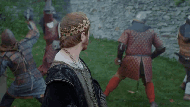 a man with a crown on his head stands in front of a group of warriors
