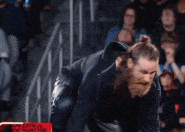 a man with a beard is standing in front of a crowd with a sign that says jami zayn vs. ew mantyre