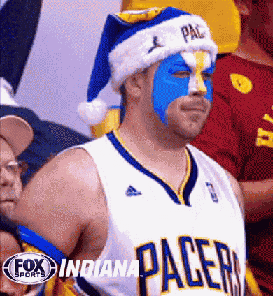 an indiana pacers fan wearing a santa hat and blue paint on his face