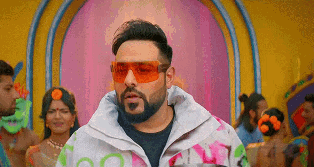 a man wearing sunglasses and a colorful jacket stands in front of a group of people