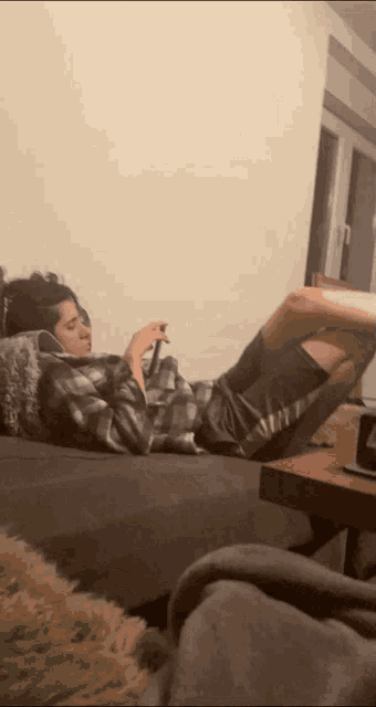 a man is laying on a couch with his legs crossed and looking at his phone