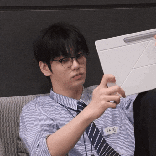 a man wearing glasses and a name tag that says 사원 looks at a tablet