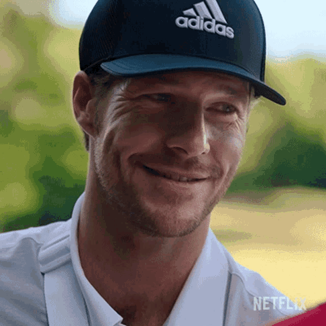 a man wearing an adidas hat is smiling