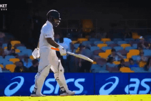 a cricket player is swinging a bat in front of an ad for asics .