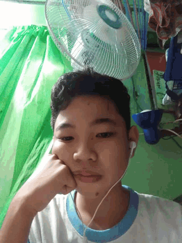 a young boy wearing ear buds and a fan looks at the camera