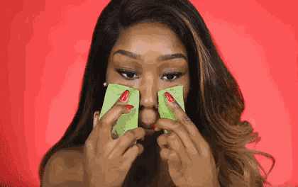 a woman with red nails is holding a green piece of paper to her face