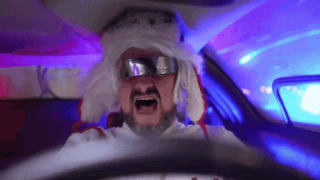 a man with a beard wearing a hat and goggles is driving a car ..