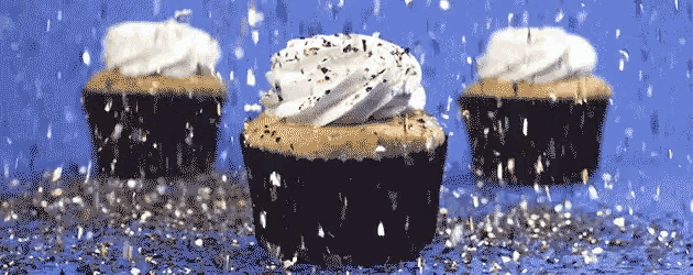three cupcakes with whipped cream on top are surrounded by confetti on a blue surface