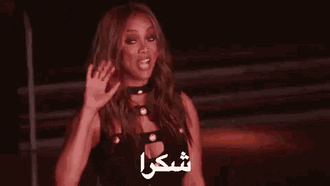 a woman in a black dress is waving her hand in front of a dark background .
