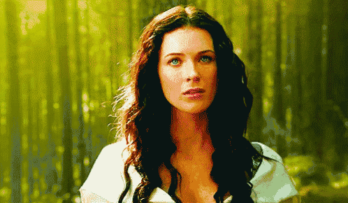 a woman with long red hair is standing in the woods