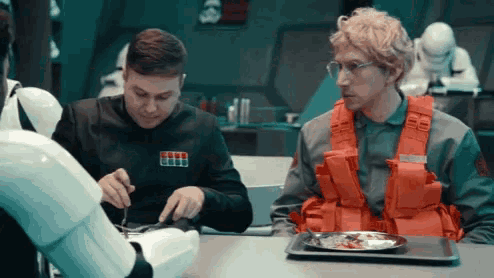 two men are sitting at a table with a robot and a plate of food ..