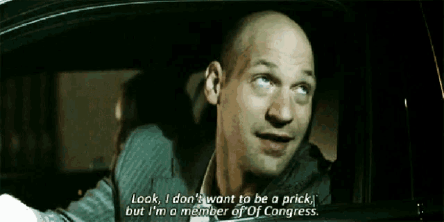 a bald man in a suit is driving a car and says look i don t want to be a prick