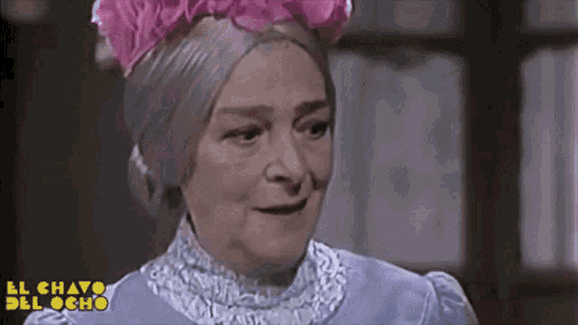 an elderly woman wearing a purple dress and a pink flower headband is smiling .