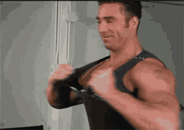 a man with a tattoo on his arm is wearing a tank top and smiling .