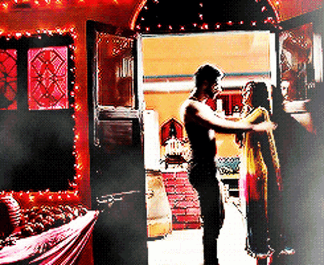 a man and woman are dancing in a room with christmas lights on the walls