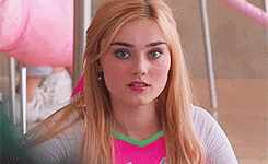 a young woman with long blonde hair is sitting in a classroom wearing a pink shirt .