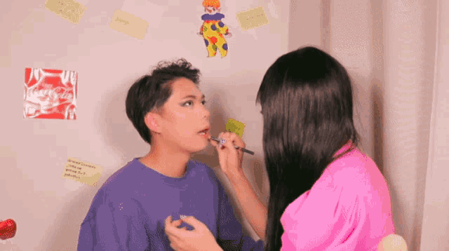 a woman applying makeup to a man with a coca-cola sticker on the wall behind them