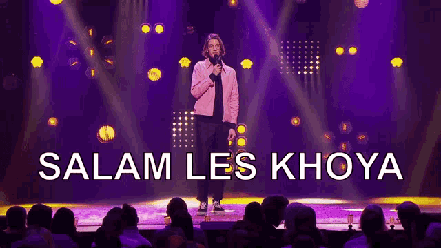 a man stands on a stage with a microphone in front of a crowd and the words salam les khoya below him