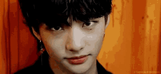 a close up of a young man 's face with a black haircut and earrings .
