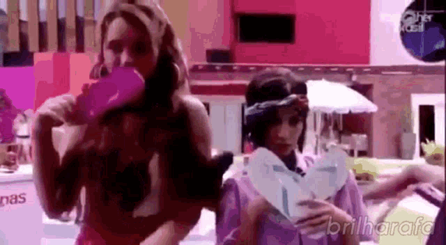 a woman is holding a pair of flip flops while another woman drinks from a pink bottle .