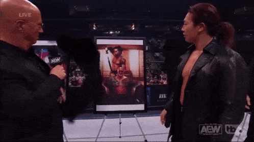 a man in a black leather jacket is talking to another man in front of a picture that says availa