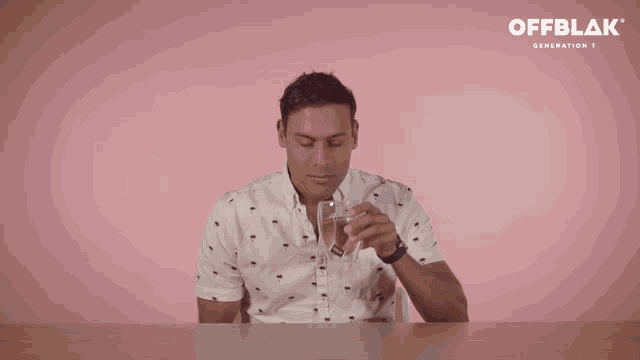 a man sits at a table with a pink background and the word offblak on the bottom