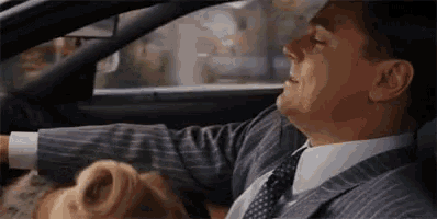 a man in a suit and tie is driving a car while a woman is sitting in the back seat .