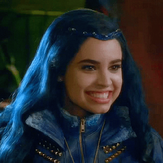 a woman with blue hair is smiling and wearing a blue jacket and necklace .