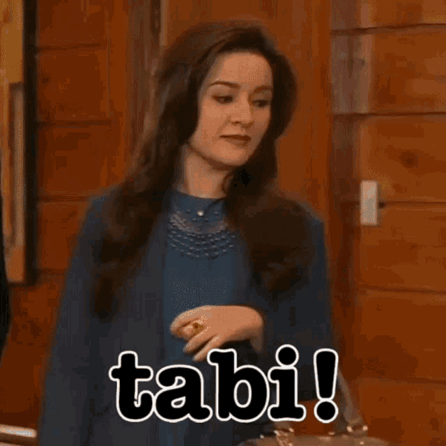 a woman in a blue jacket is standing in front of a wooden door with the word tabi written on it