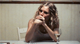 a woman sits at a table with a glass of wine on it