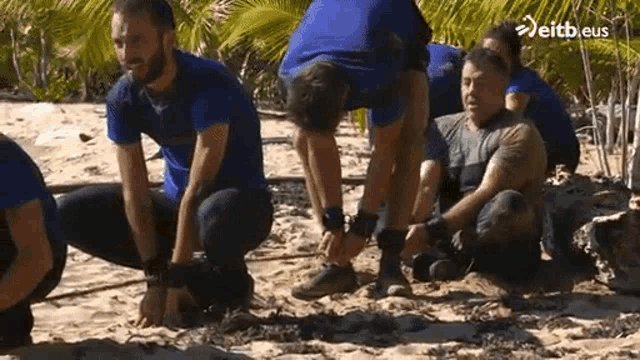 a group of men are squatting down on a beach .
