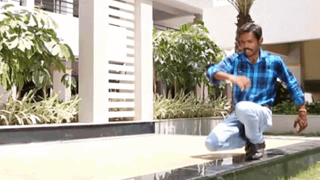 a man in a blue plaid shirt is kneeling down on a sidewalk