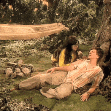 a man and woman are laying under a tree with a hammock in the background
