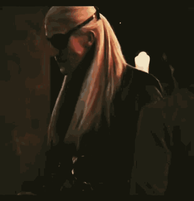 a man with long blonde hair wearing sunglasses and a blindfold is standing next to another man .