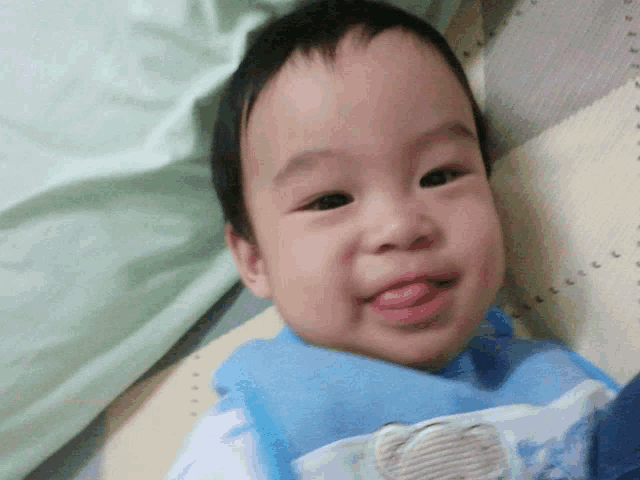 a baby is sticking his tongue out while wearing a blue bib