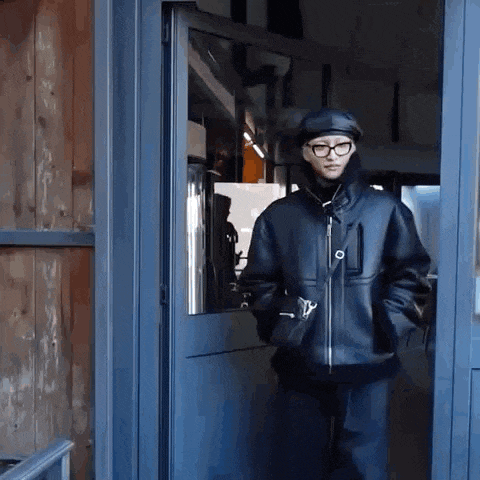 a man wearing glasses and a hat is standing in a doorway .