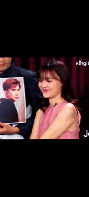 a woman in a pink dress is smiling while holding a picture of a man 's face
