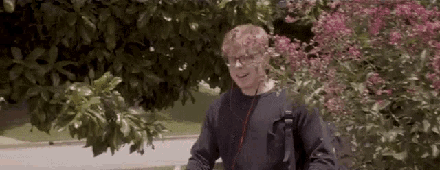 a man wearing headphones and a black shirt is standing in front of a bush with pink flowers .