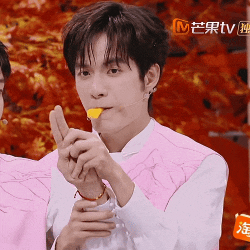 a man wearing a pink vest is holding a piece of food in his mouth