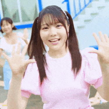 a girl in a pink shirt is waving her hands and smiling