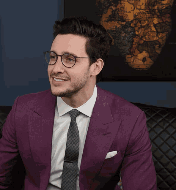 a man in a purple suit and tie smiles in front of a map of the world