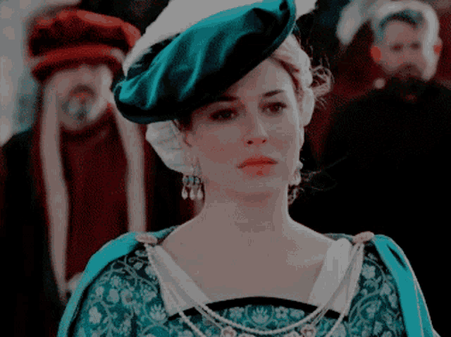 a woman wearing a green hat and a blue dress looks at the camera