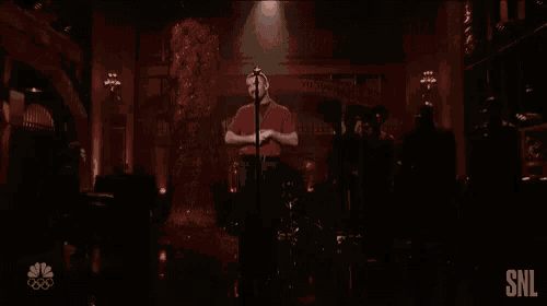 a man singing into a microphone with a snl logo in the corner