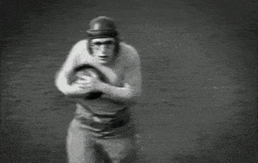 a black and white photo of a football player holding a ball on a field .