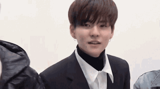 a young man in a suit and turtleneck is standing next to another man .