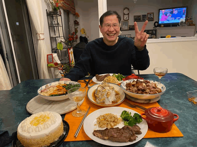 a man sitting at a table with plates of food and a cake that says birthday on it